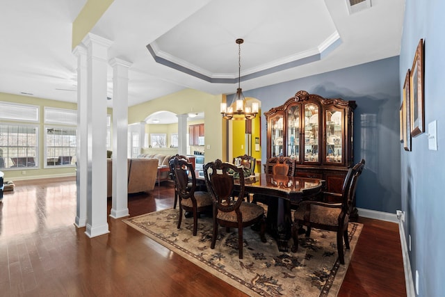 dining space with a raised ceiling, visible vents, dark wood-style flooring, and ornate columns