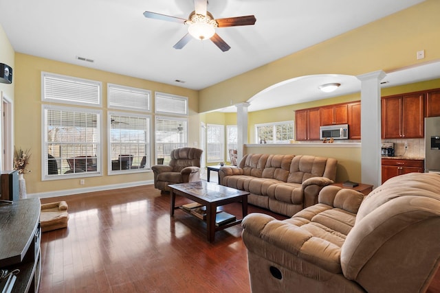 living room with dark wood-type flooring, a ceiling fan, visible vents, and ornate columns