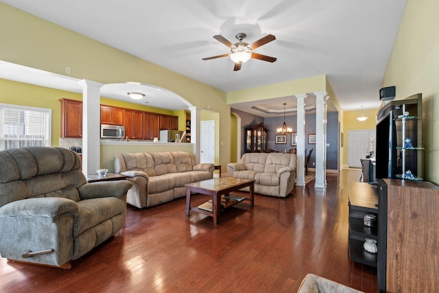 living room featuring dark wood-type flooring, decorative columns, ceiling fan with notable chandelier, and arched walkways