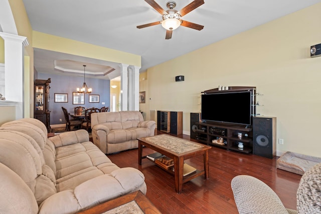 living room featuring baseboards, ornate columns, dark wood-style flooring, a raised ceiling, and ceiling fan with notable chandelier