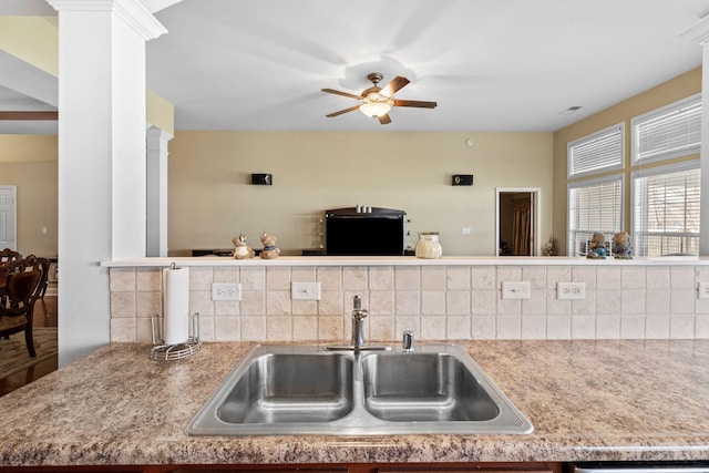 kitchen with ornate columns, ceiling fan, a sink, light countertops, and tasteful backsplash