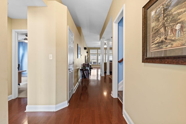 hallway with stairway, baseboards, dark wood finished floors, and ornate columns