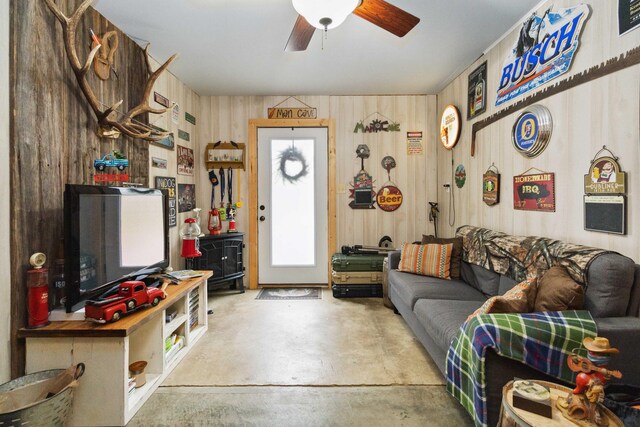 living room with wood walls, concrete floors, and ceiling fan