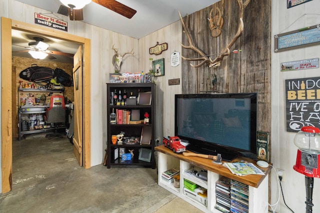 living room featuring wooden walls, ceiling fan, and concrete floors