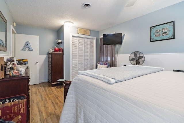 bedroom with a textured ceiling, light wood-type flooring, ceiling fan, and a closet