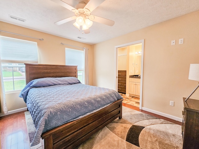 bedroom featuring light wood-type flooring, a textured ceiling, ceiling fan, and ensuite bath