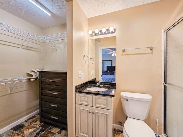 bathroom with toilet, vanity, a textured ceiling, and a shower with shower door