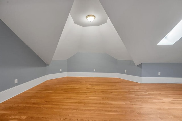 additional living space featuring light wood-type flooring and lofted ceiling with skylight