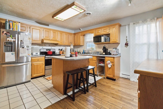 kitchen with a baseboard heating unit, stainless steel appliances, a textured ceiling, a kitchen island, and light wood-type flooring