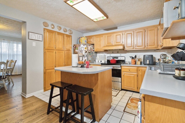 kitchen featuring appliances with stainless steel finishes, a kitchen breakfast bar, a textured ceiling, a kitchen island, and light wood-type flooring