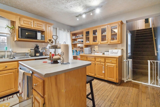 kitchen with a textured ceiling, a kitchen bar, sink, light hardwood / wood-style floors, and a center island