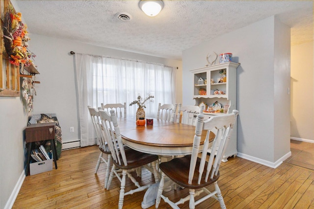 dining area featuring a textured ceiling, light hardwood / wood-style flooring, and a baseboard heating unit