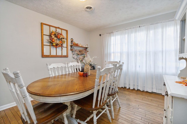 dining room with light wood-type flooring and a textured ceiling