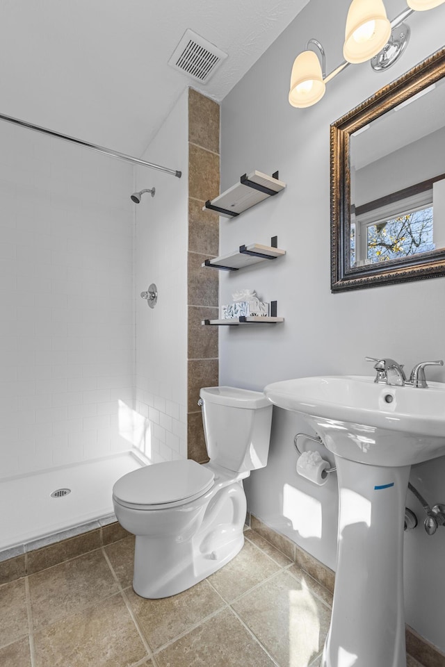 bathroom featuring tile patterned flooring, a tile shower, and toilet