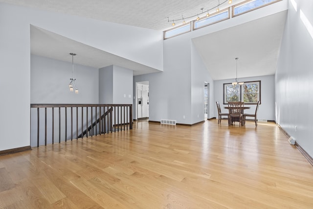 unfurnished room with an inviting chandelier, track lighting, light hardwood / wood-style flooring, and a high ceiling