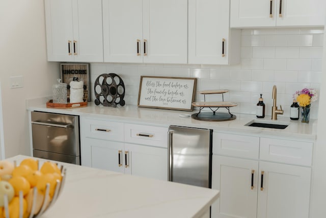 kitchen with white cabinets, backsplash, stainless steel refrigerator, and sink