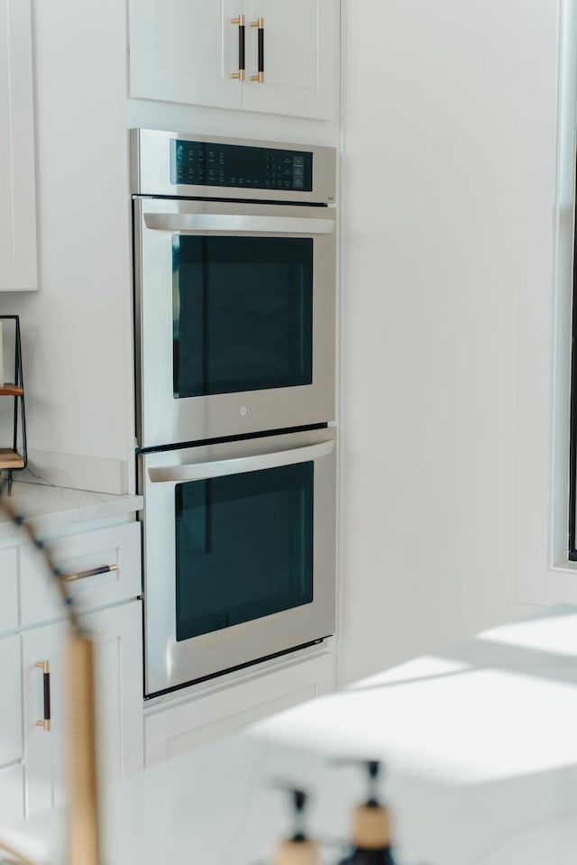 kitchen with stainless steel double oven, white cabinetry, and light stone counters