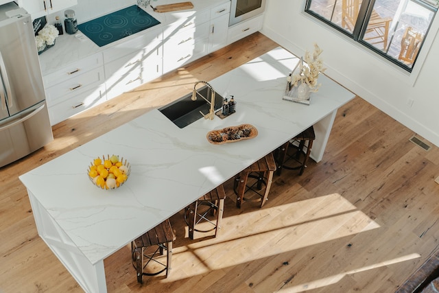 kitchen with light stone countertops, light wood-type flooring, white cabinetry, and stainless steel refrigerator