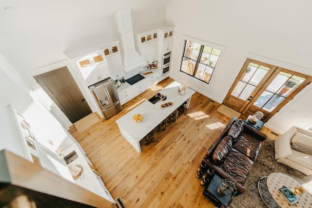 living room with plenty of natural light, a towering ceiling, french doors, and light hardwood / wood-style flooring