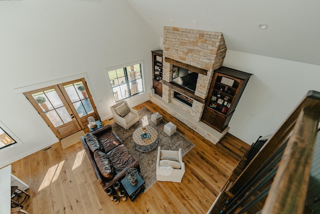 living room with a fireplace, wood-type flooring, high vaulted ceiling, and french doors