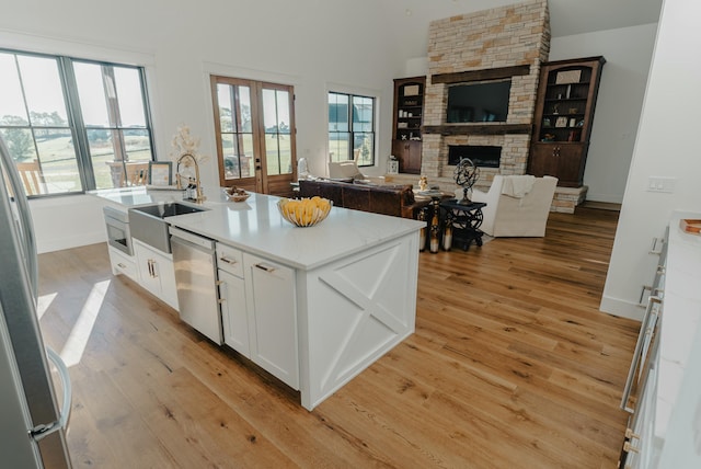 kitchen with stainless steel appliances, a fireplace, white cabinets, a center island with sink, and light wood-type flooring