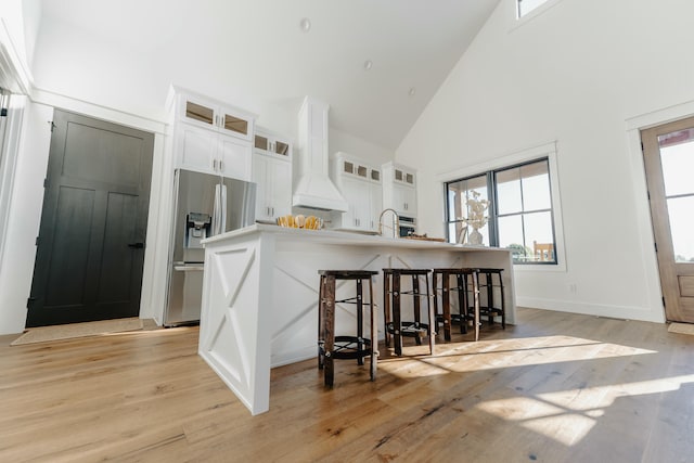 kitchen featuring white cabinetry, light hardwood / wood-style flooring, high vaulted ceiling, stainless steel refrigerator with ice dispenser, and custom range hood