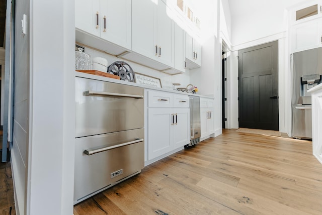 kitchen featuring stainless steel fridge, white cabinetry, light wood-type flooring, and wine cooler