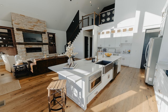 kitchen with sink, stainless steel appliances, an island with sink, white cabinets, and light wood-type flooring