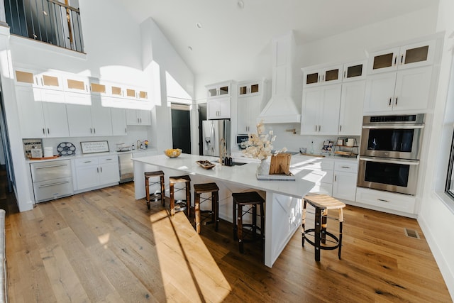 kitchen with a kitchen breakfast bar, light wood-type flooring, stainless steel appliances, a kitchen island with sink, and white cabinets