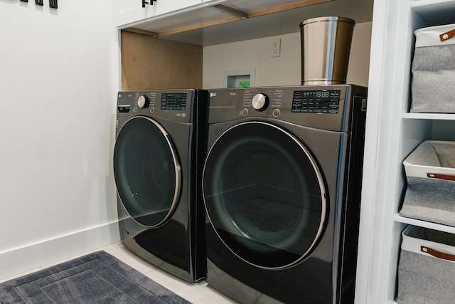 laundry area featuring washing machine and dryer, light tile patterned flooring, and cabinets