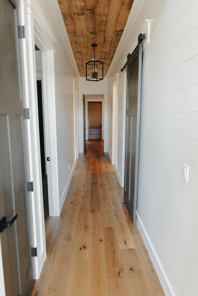 hall with a barn door, light wood-type flooring, wooden ceiling, and an inviting chandelier