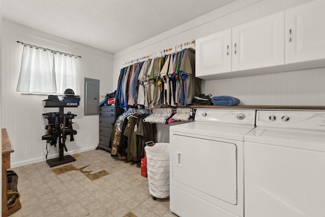 clothes washing area with electric panel, cabinets, a textured ceiling, wooden walls, and washing machine and dryer