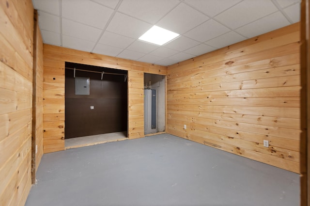 unfurnished bedroom featuring electric water heater, concrete flooring, wooden walls, and a paneled ceiling