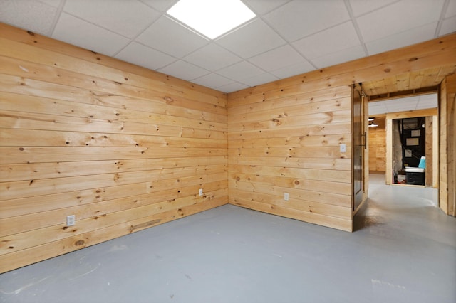 spare room with a drop ceiling, wooden walls, and concrete floors