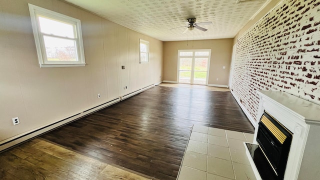 unfurnished living room with a baseboard heating unit, wood-type flooring, ceiling fan, a large fireplace, and brick wall