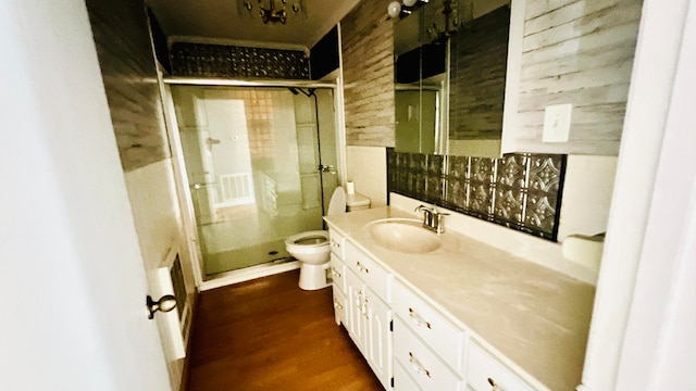 bathroom with wood walls, a shower with door, wood-type flooring, vanity, and toilet