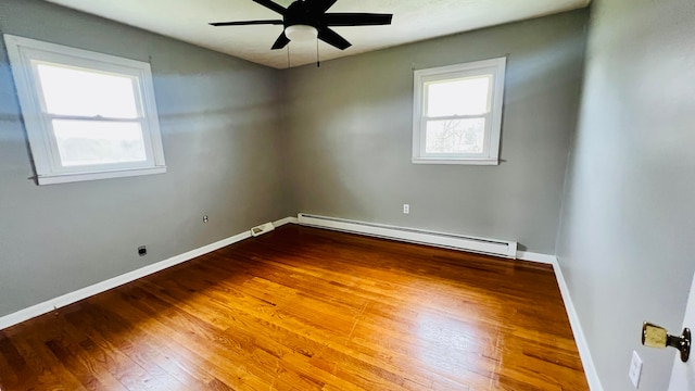 empty room with a wealth of natural light, hardwood / wood-style floors, ceiling fan, and a baseboard radiator