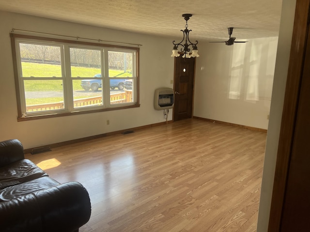 living area featuring light wood-type flooring, heating unit, baseboards, a textured ceiling, and a chandelier
