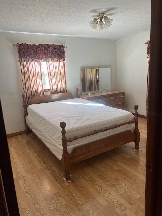 bedroom featuring a textured ceiling, light wood-style floors, and baseboards