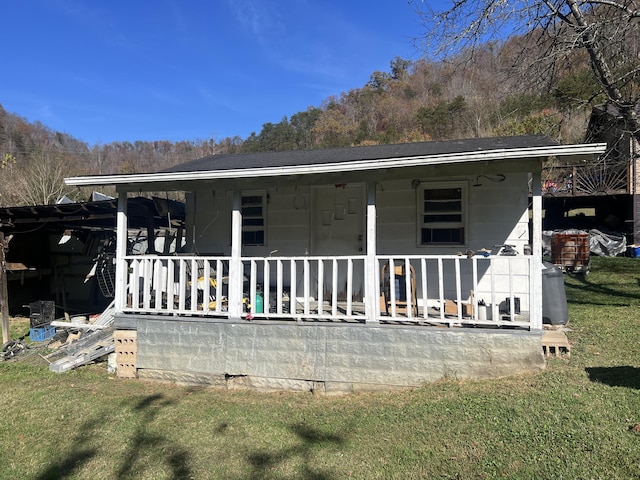 back of house with a porch, a yard, and a shingled roof