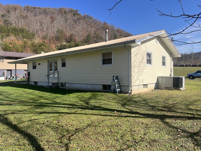 back of property featuring central air condition unit, metal roof, and a lawn