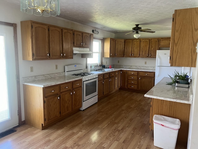 kitchen featuring white appliances, under cabinet range hood, brown cabinets, a chandelier, and a textured ceiling