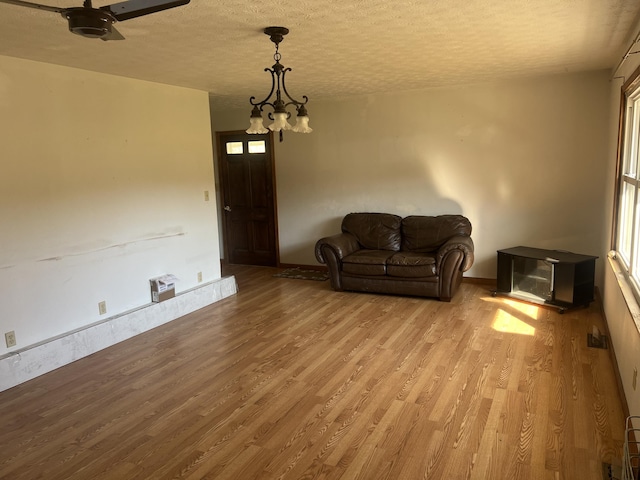 unfurnished living room featuring wood finished floors, a textured ceiling, a chandelier, and a ceiling fan