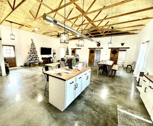 kitchen with a breakfast bar, a towering ceiling, a barn door, open floor plan, and wood counters