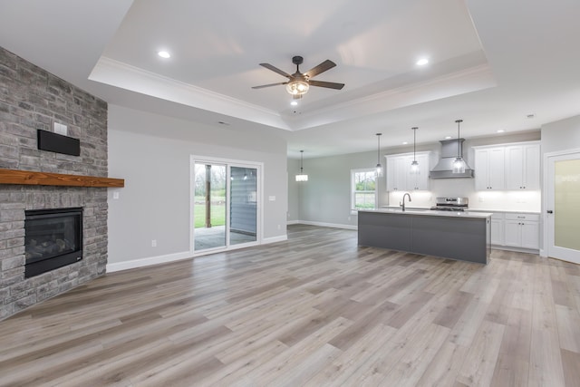 kitchen featuring a raised ceiling, a kitchen island with sink, white cabinets, and wall chimney range hood