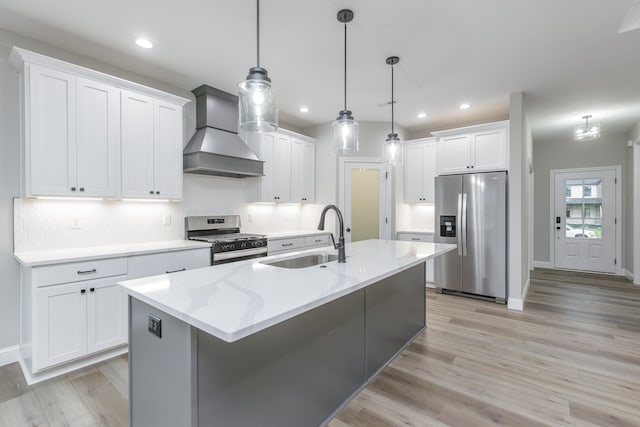 kitchen with appliances with stainless steel finishes, sink, wall chimney range hood, pendant lighting, and white cabinetry