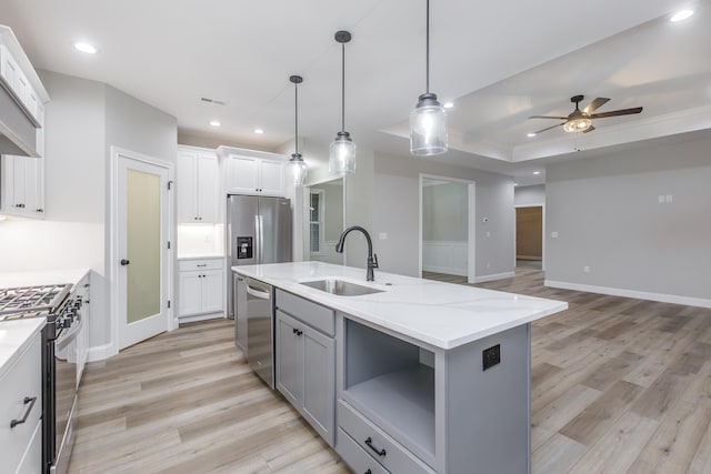 kitchen featuring a kitchen island with sink, sink, appliances with stainless steel finishes, decorative light fixtures, and white cabinetry