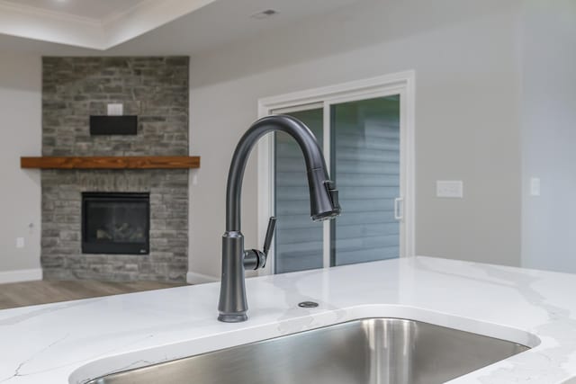 room details featuring light stone counters, ornamental molding, sink, a fireplace, and hardwood / wood-style floors