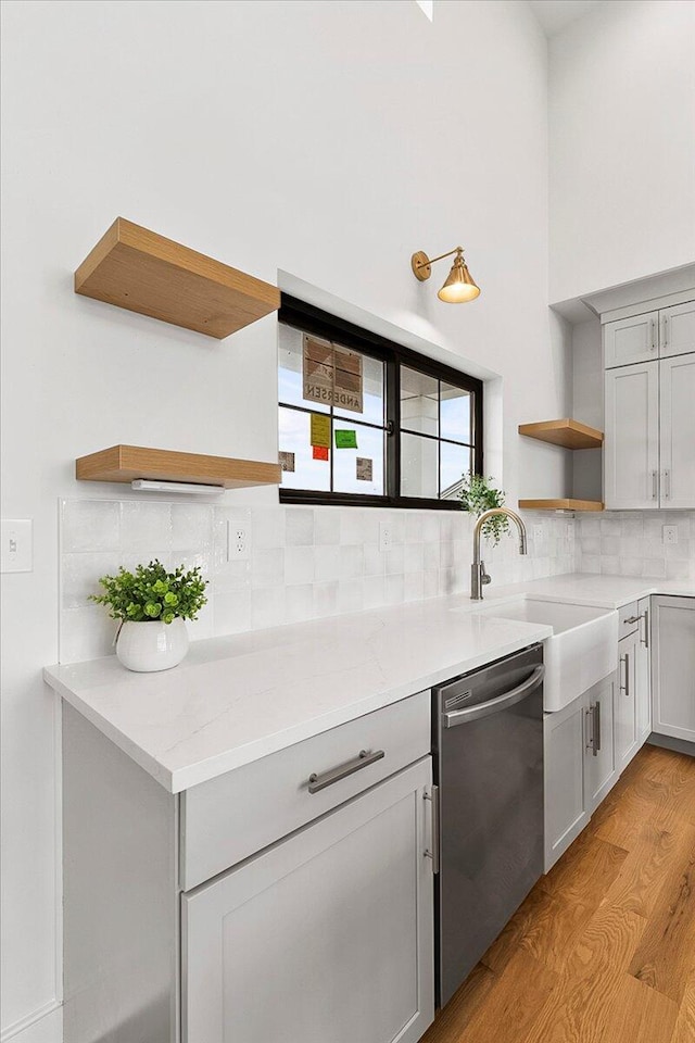 kitchen featuring stainless steel dishwasher, light stone counters, open shelves, decorative backsplash, and light wood-type flooring