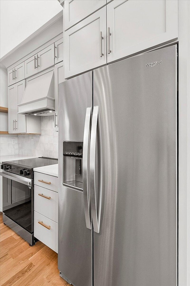 kitchen with light wood-style flooring, open shelves, appliances with stainless steel finishes, decorative backsplash, and custom exhaust hood